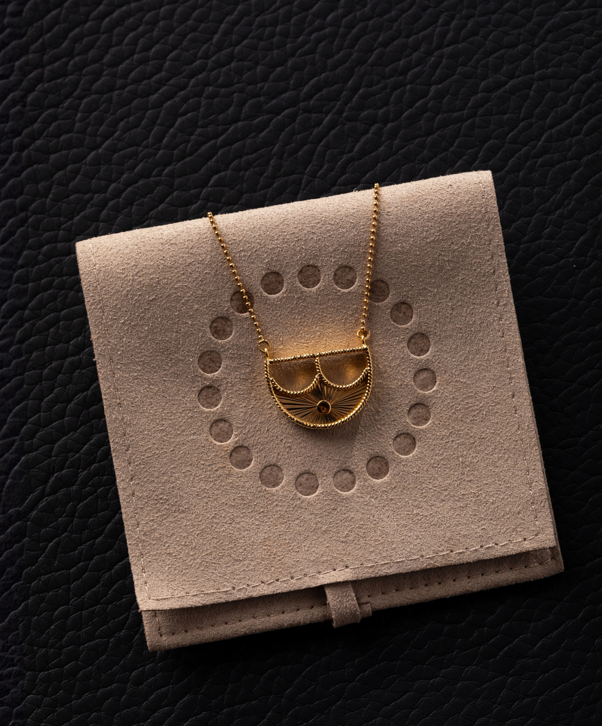 Gold necklace on a beige jewelry display box against a black textured background