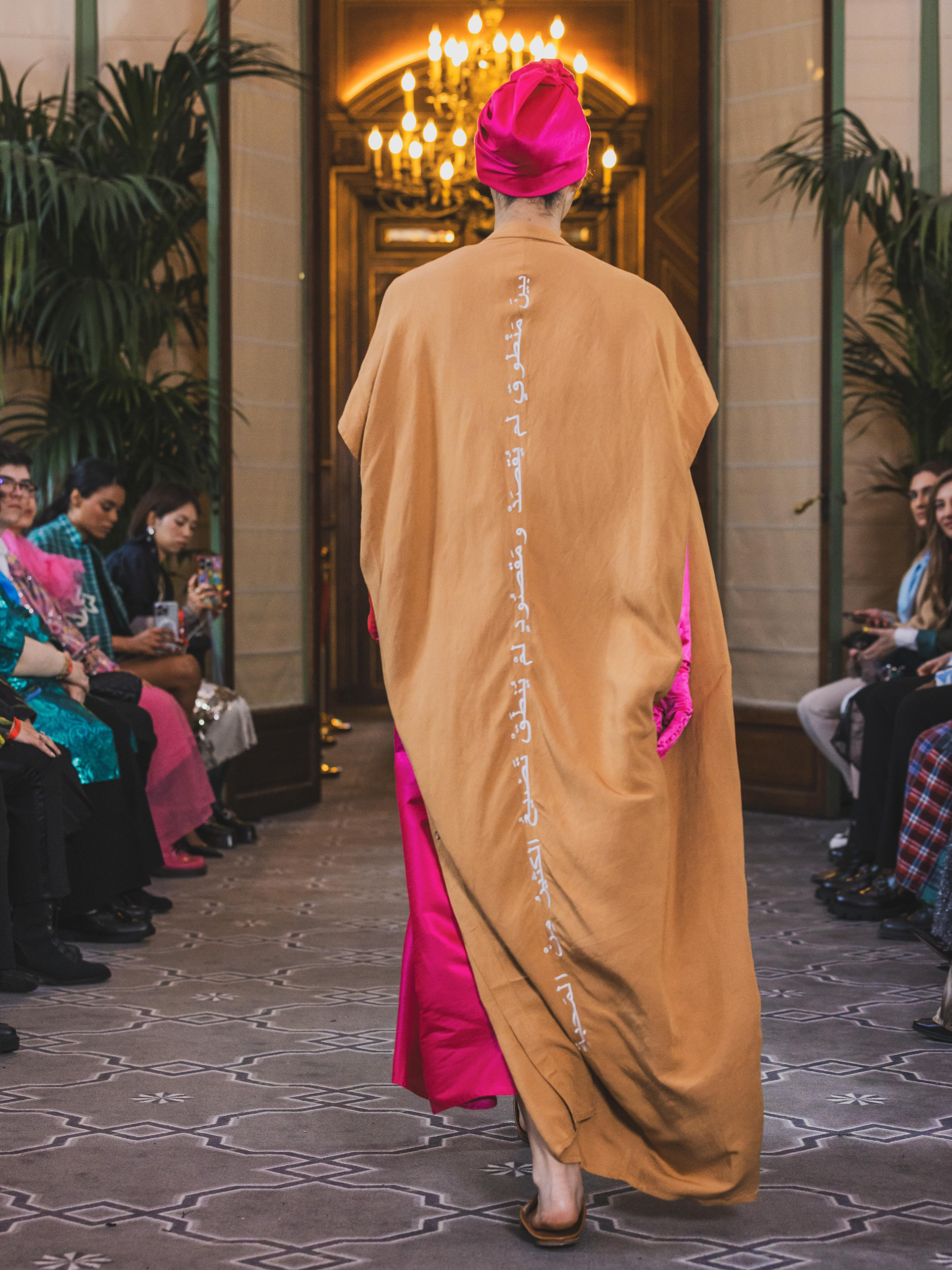 Model walking in camel kaftan back view showcasing Arabic embroidery designed by Omni The Label KSA UAE Qatar
