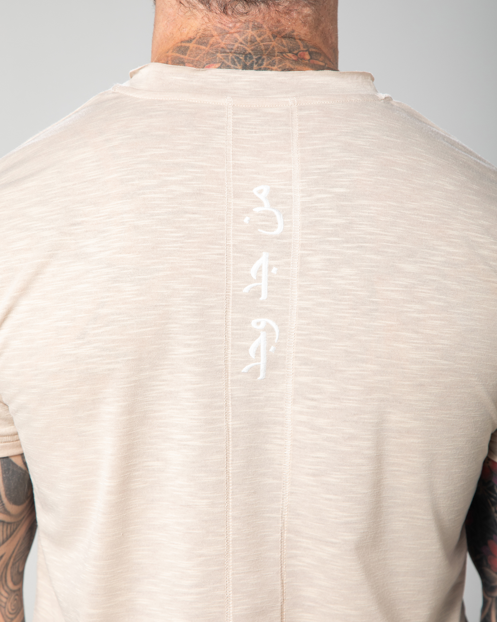 lose-up of the Marbella nude T-shirt showcasing vertical Arabic calligraphy reading “Who seeks, finds,” embroidered with intention for a meaningful finishing touch UAE KSA Qatar
