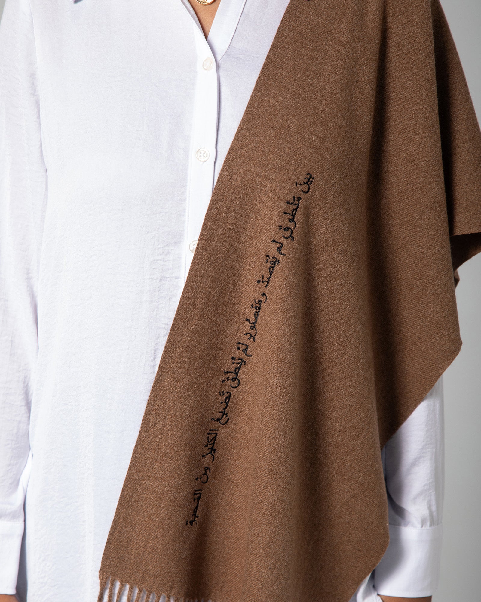 Close-up of Arabic calligraphy embroidery on brown scarf with soft woven texture – UAE, KSA, Qatar