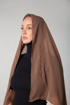 A woman wearing a brown scarf with black embroidery.