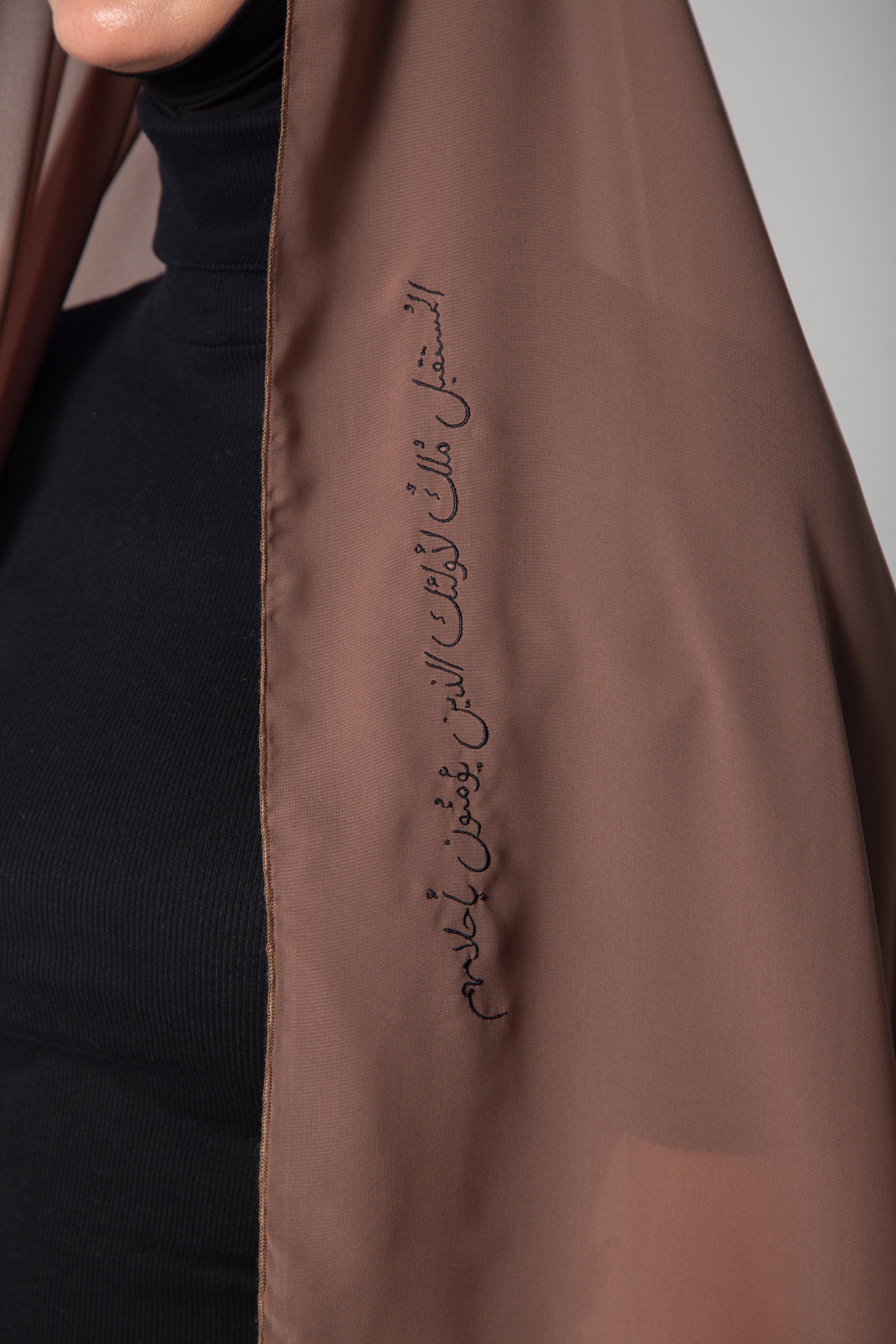 A woman wearing a brown scarf with  embroidery  paired with a black outfit KSA UAE Qatar