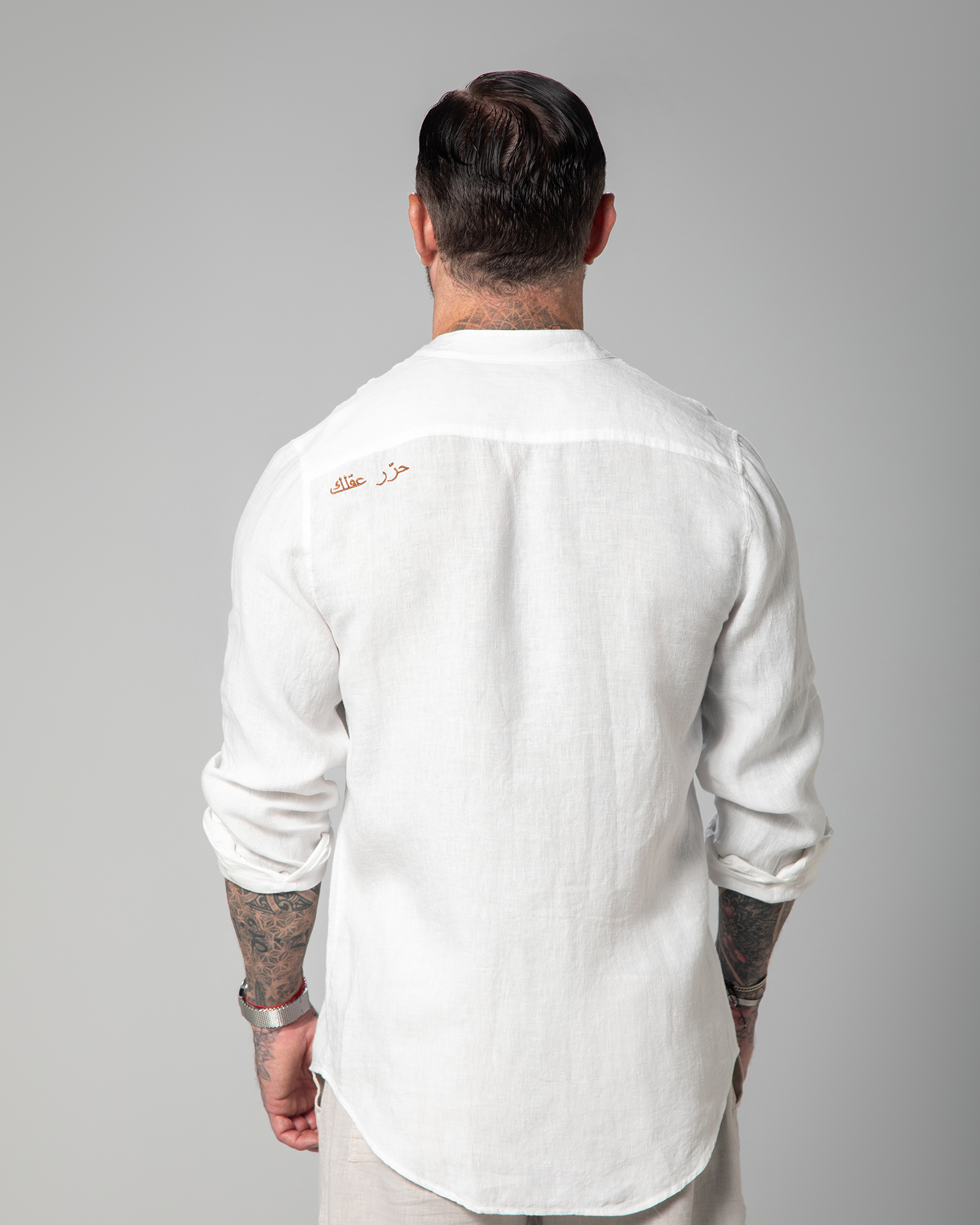 A man wearing a white linen shirt with half-hidden front buttons and 'Free Your Mind' embroidery on the back left side.