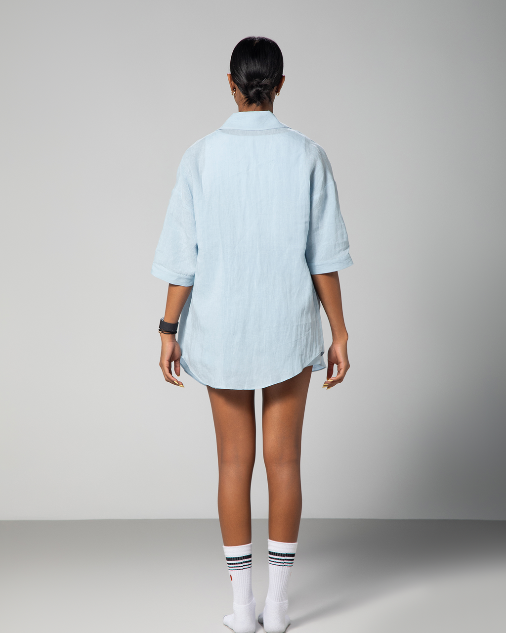 Back view of a woman wearing a baby blue linen co-ord set from Omni The Label, showcasing the relaxed fit and subtle embroidery detail on the shirt, styled for modern summer comfort UAE KSA Qatar
