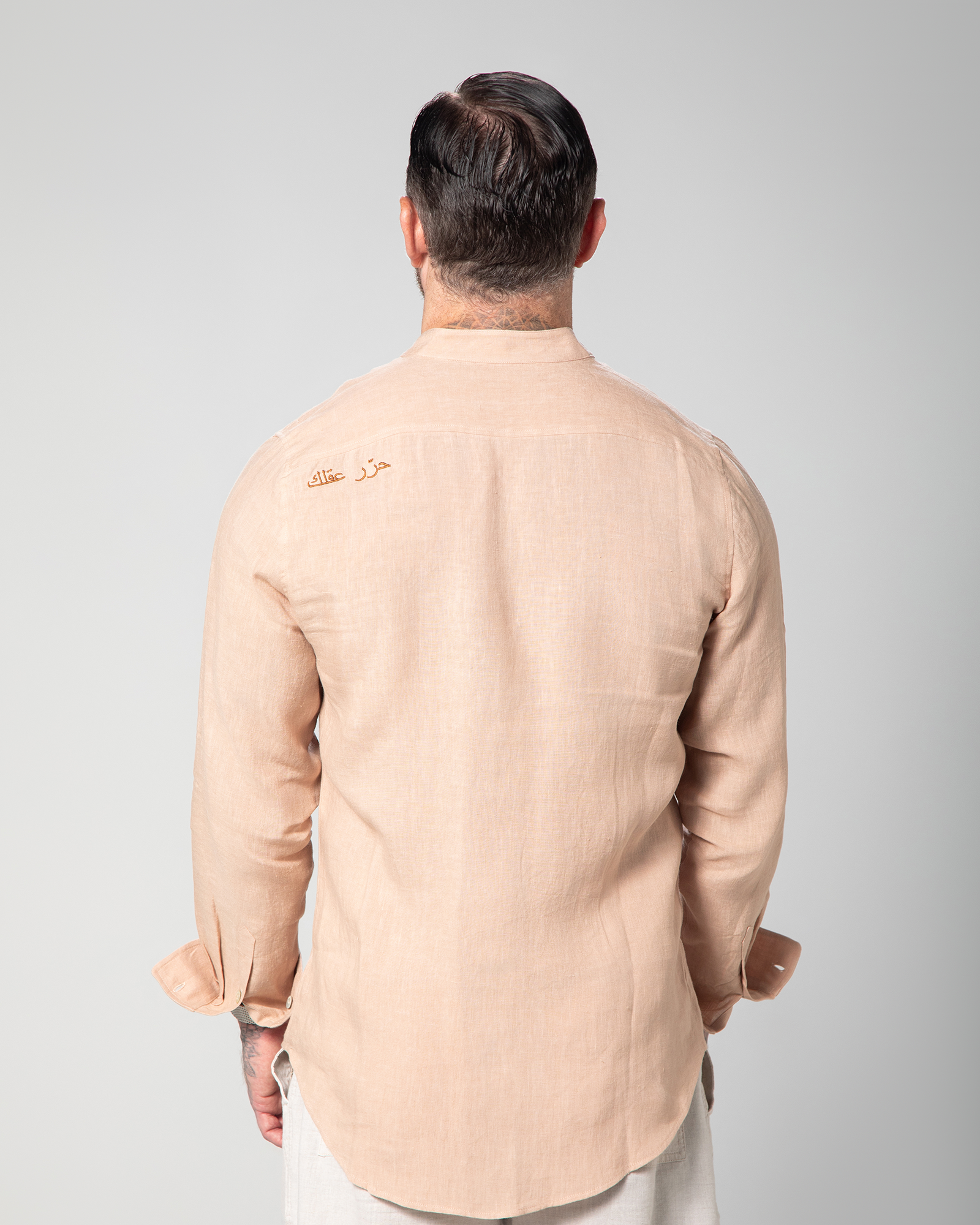 Back view of model wearing the nude St. Tropez linen shirt with Arabic embroidery reading "Free Your Mind" on the upper left side KMale model walking in the Marbella nude T-shirt by Omni The Label with Arabic embroidery reading this too shall pass shown in motion to highlight soft lightweight slub jersey fabric ideal for UAE KSA Qatar
