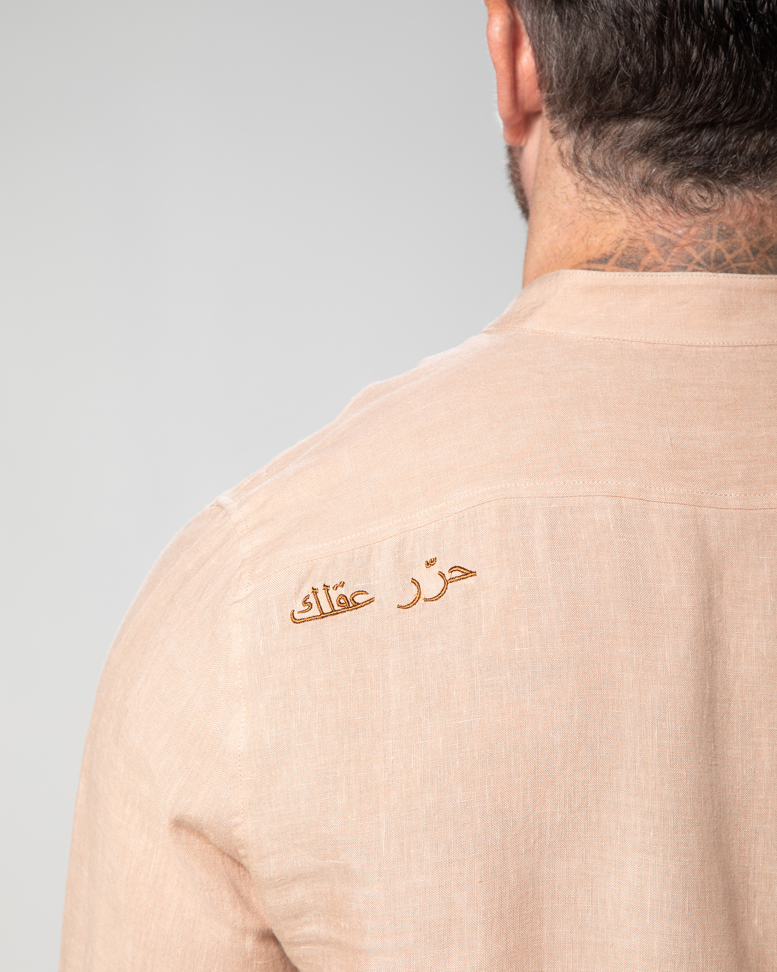 Close-up of Arabic embroidery on the back of the nude St. Tropez linen shirt, reading "Free Your Mind" in elegant script Male model walking in the Marbella nude T-shirt by Omni The Label with Arabic embroidery reading this too shall pass shown in motion to highlight soft lightweight slub jersey fabric ideal for UAE KSA Qatar
