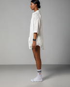 Side view of a model wearing Omni The Label’s white linen co-ord set, showcasing the loose-fit short-sleeve shirt and flowy shorts with a relaxed, effortless drape.UAE, KSA, Qatar