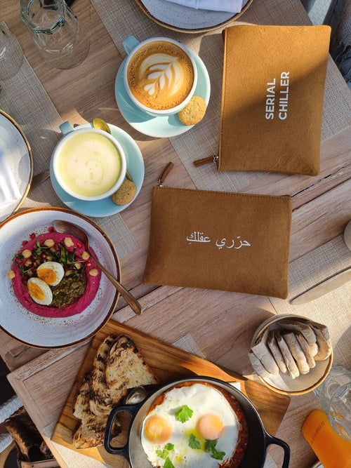 Minimalist brown fit zipper pouch with Arabic print free your mind, styled with breakfast setting — perfect for daily essentials.UAE, KSA, Qatar